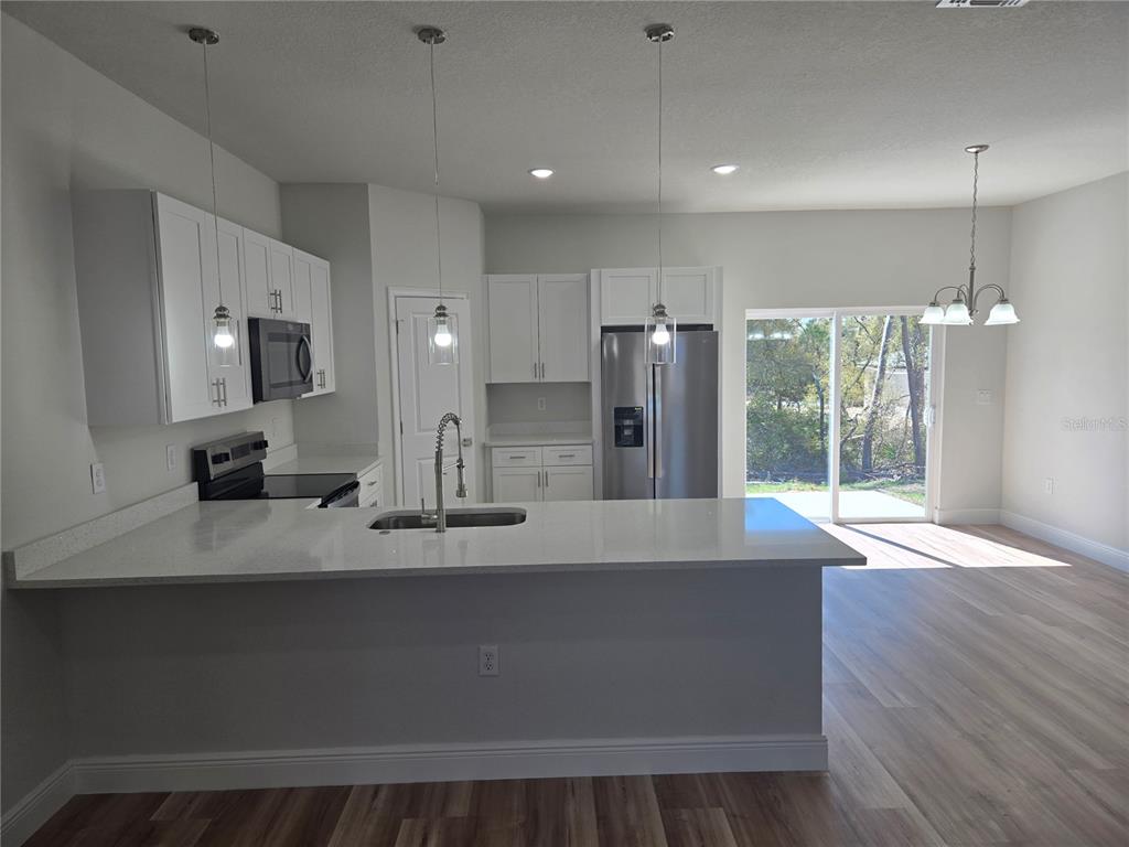 3862 Southwest 147th Street Ocala, FL 34473 - Photo 6 of 29 a large kitchen with stainless steel appliances a large counter top a refrigerator a sink a fireplace and wooden floor