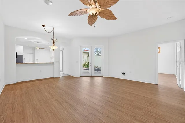 an empty room with wooden floor chandelier fan and windows
