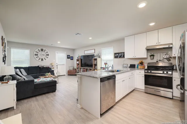 a kitchen with stainless steel appliances granite countertop a refrigerator oven a sink dishwasher and white cabinets with wooden floor