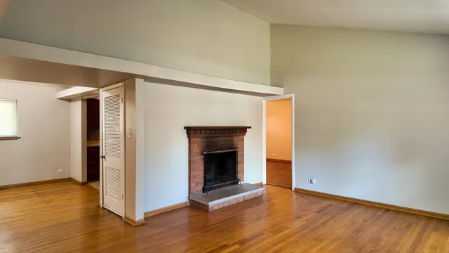 a view of an empty room with wooden floor fireplace and a window