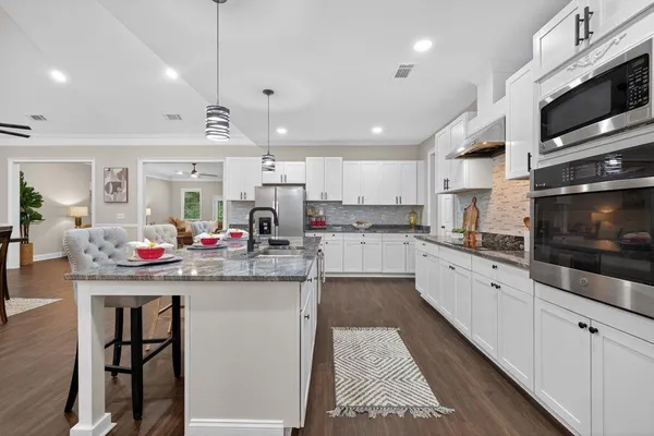 a kitchen with stainless steel appliances granite countertop a stove top oven a sink dishwasher a dining table and chairs with white cabinets