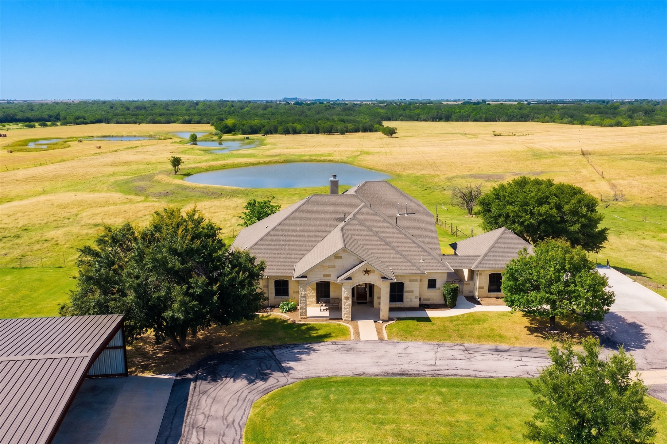 20145 Janak Road Coupland, TX 78615 - Photo 4 of 40 An aerial perspective reveals a beautiful stone home nestled amidst green fields and a placid pond.
