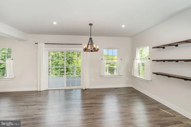 an empty room with wooden floor chandelier and windows