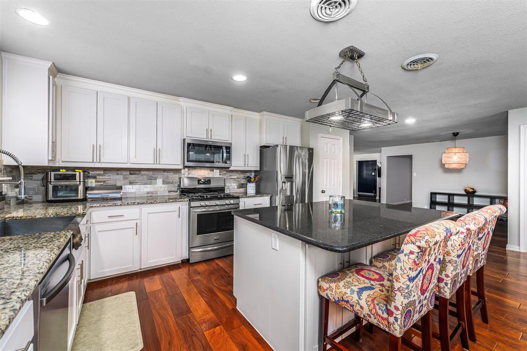 6512 Greenway Road Fort Worth, TX 76116 - Photo 11 of 38 Kitchen with a kitchen breakfast bar, a center island, dark wood-type flooring, appliances with stainless steel finishes, and dark stone countertops