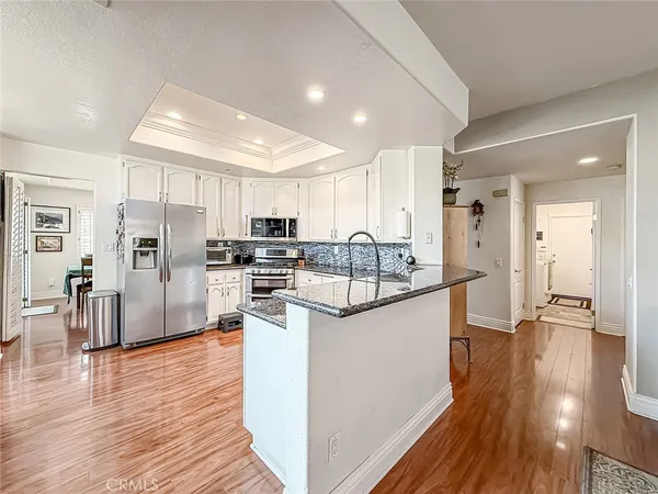 a kitchen with stainless steel appliances granite countertop a stove a refrigerator a sink a dining table and chairs with the wooden floor
