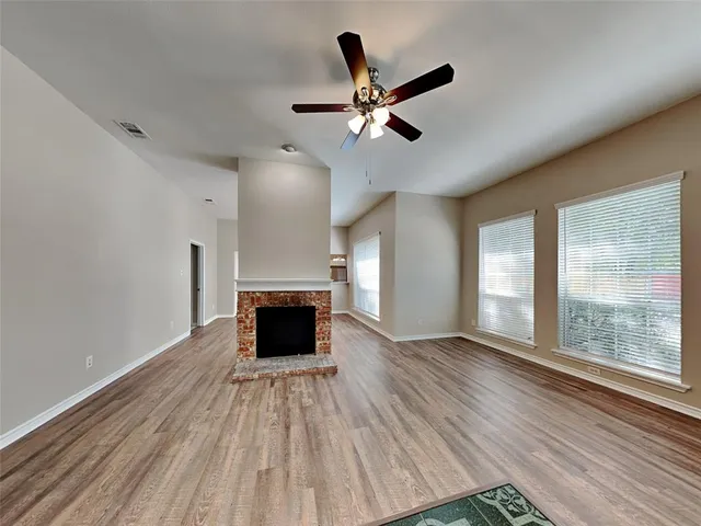 an empty room with wooden floor a ceiling fan and windows