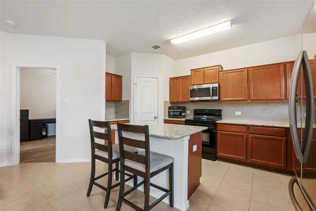 a kitchen with stainless steel appliances granite countertop a stove top oven a sink dishwasher and a refrigerator with wooden cabinets