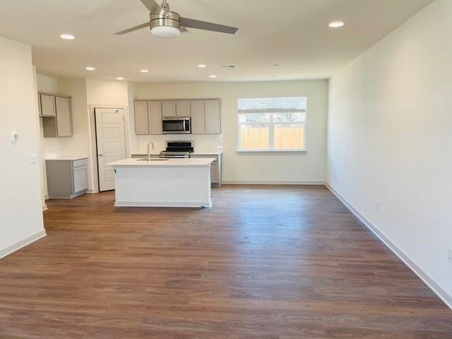 161 Filifera Court Leander, TX 78641 - Photo 4 of 13 Kitchen with appliances with stainless steel finishes, gray cabinetry, ceiling fan, a center island with sink, and dark wood-type flooring