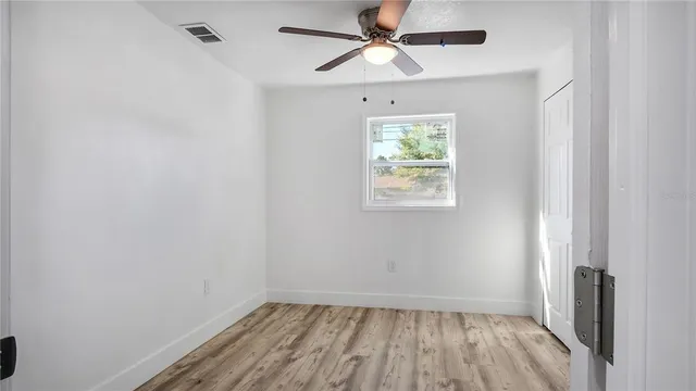 an empty room with wooden floor chandelier fan and windows