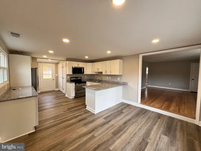 a large kitchen with kitchen island a sink dishwasher stove and white cabinets with wooden floor