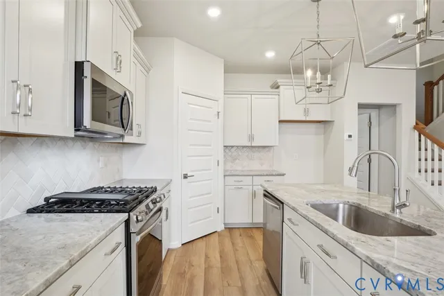 a kitchen with stainless steel appliances granite countertop a sink dishwasher a stove top oven a refrigerator with white cabinets and wooden floor