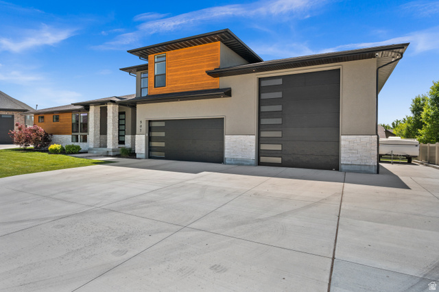 Modern home featuring stone siding, driveway, a garage, and stucco siding