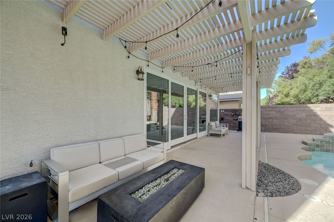 2391 Rainswept Avenue Henderson, NV 89052 - Photo 60 of 62 An inviting outdoor patio features a pergola, a fire pit, and glass sliding doors leading indoors.