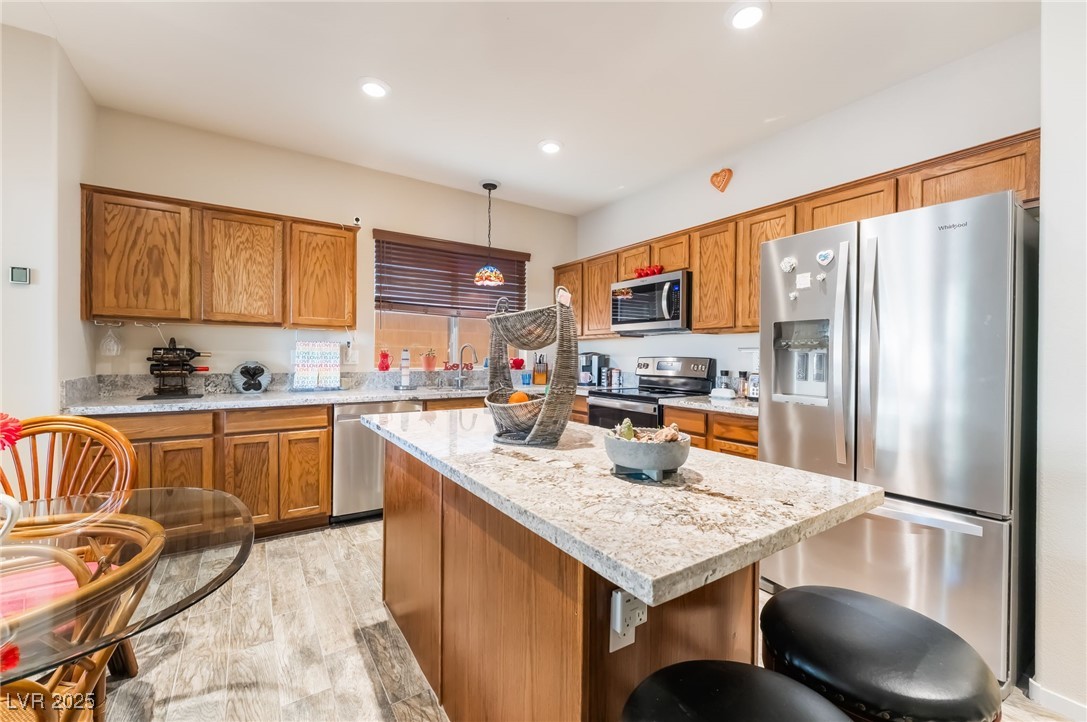 4732 Adriano Way Pahrump, NV 89061 - Photo 17 of 44 Kitchen with stainless steel appliances, brown cabinets, light stone counters, light wood finished floors, and a center island
