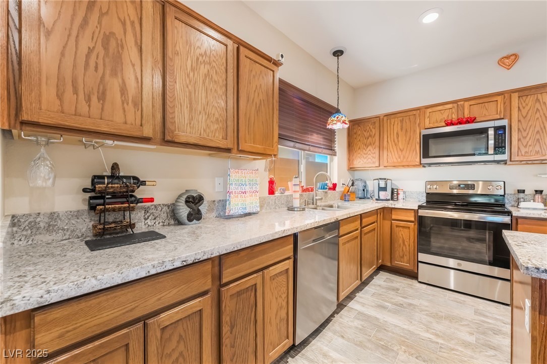 4732 Adriano Way Pahrump, NV 89061 - Photo 19 of 44 Kitchen featuring brown cabinets, decorative light fixtures, stainless steel appliances, light stone countertops, and light wood-style flooring