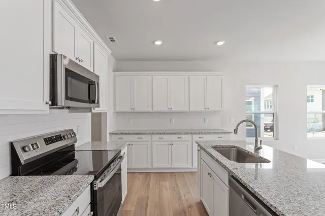 a kitchen with granite countertop a sink dishwasher stove and white cabinets with wooden floor