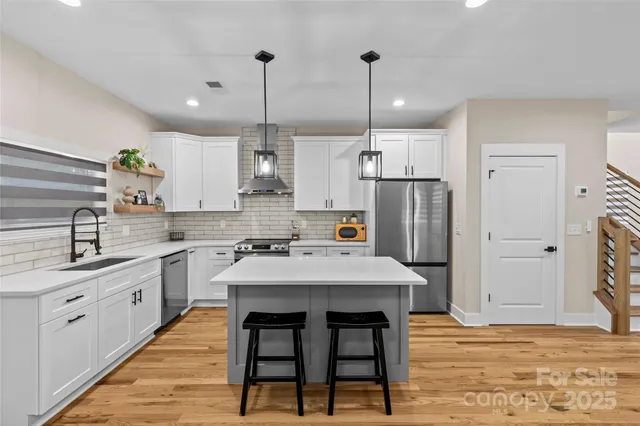 a kitchen with stainless steel appliances kitchen island granite countertop a sink a stove a refrigerator and island with wooden floor