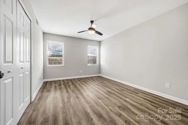 an empty room with wooden floor ceiling fan and windows