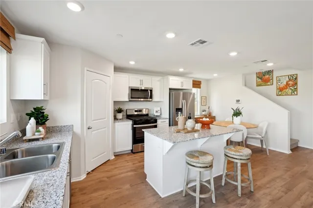 a kitchen with stainless steel appliances kitchen island granite countertop a dining table chairs refrigerator and sink