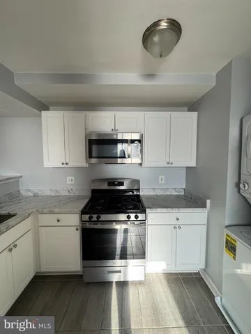 a white kitchen with granite countertop a stove top oven a sink a counter space and cabinets