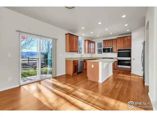 a kitchen with stainless steel appliances granite countertop a stove top oven a sink dishwasher a refrigerator and a dining table with wooden floor