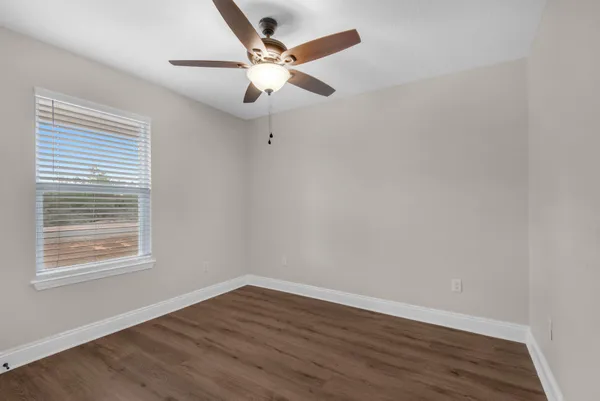 an empty room with wooden floor fan and windows