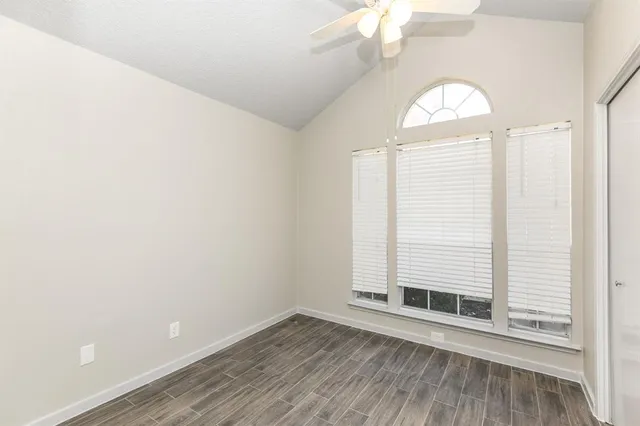 an empty room with wooden floor fan and windows