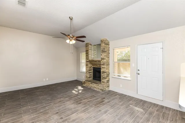 an empty room with wooden floor fireplace and windows
