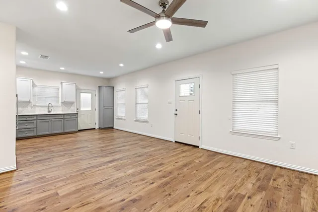 an empty room with wooden floor a ceiling fan and kitchen view