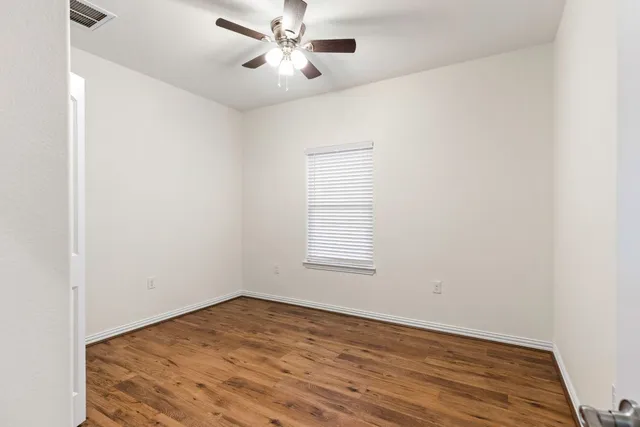 an empty room with wooden floor fan and windows