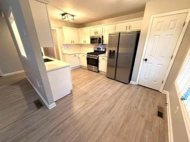 a kitchen with stainless steel appliances a refrigerator a sink dishwasher a stove and white countertops with wooden floor