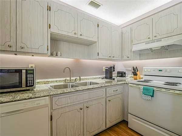 a kitchen with stainless steel appliances granite countertop a sink dishwasher stove and white cabinets