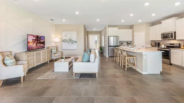 a living room with stainless steel appliances furniture a rug and a kitchen view
