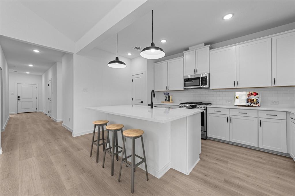 1509 Hamilton Street Howe, TX 75459 - Photo 7 of 23 Kitchen with tasteful backsplash, appliances with stainless steel finishes, light countertops, light wood finished floors, and a kitchen breakfast bar