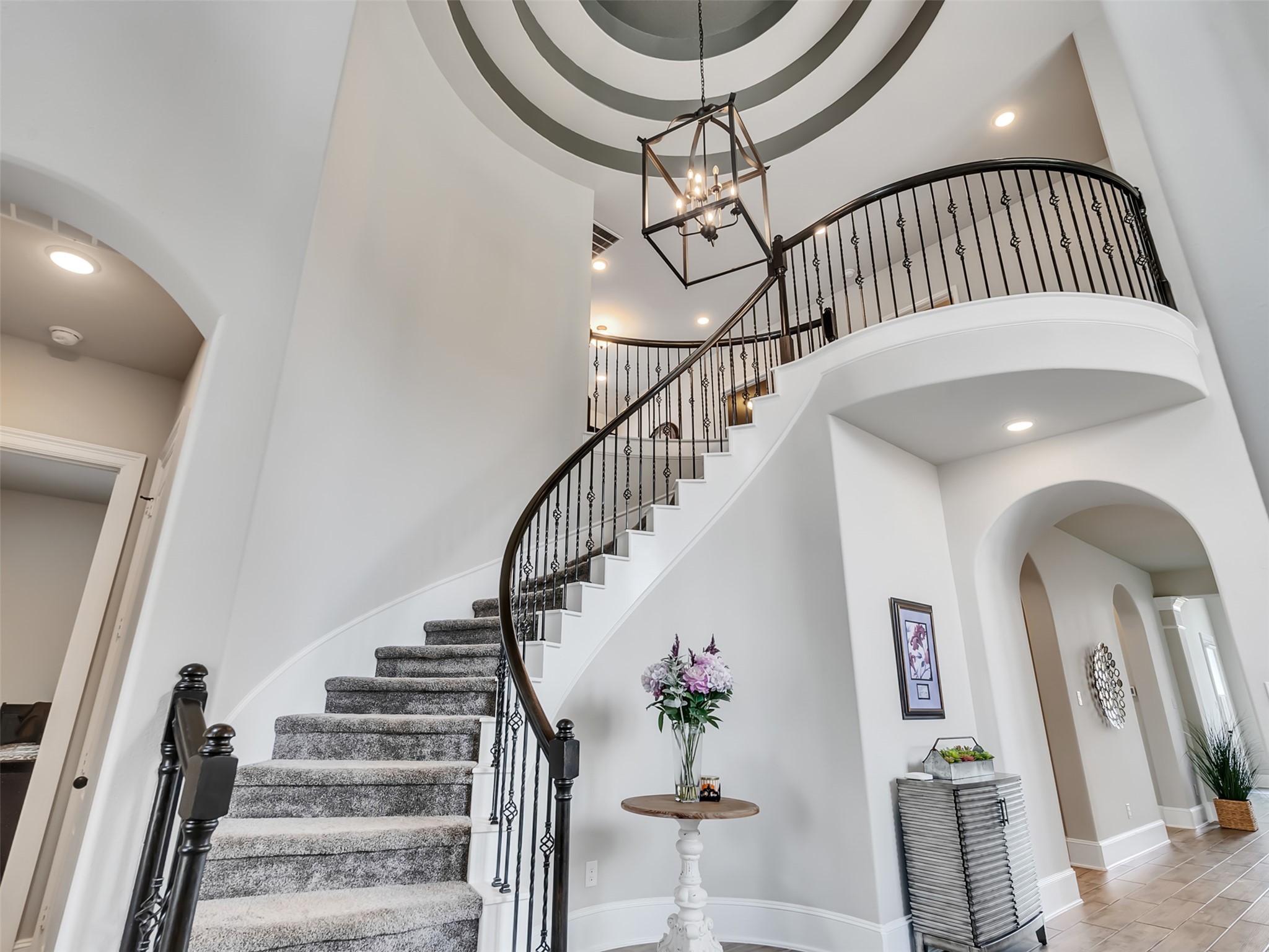 10302 Muir Peak Drive Rosharon, TX 77583 - Photo 4 of 40 A curved staircase with iron railings, a high ceiling with a stylish light fixture, and neutral tones.