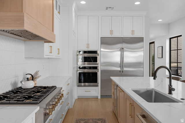 5367 Cyan Lane St. George, UT 84790 - Photo 27 of 49 Gourmet kitchen featuring a built-in stainless steel refrigerator, double wall ovens, a large gas range with a wood-finish vent hood, a spacious island with an undermount sink and matte black faucet, and light wood-finish flooring