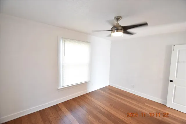 an empty room with wooden floor ceiling fan and windows