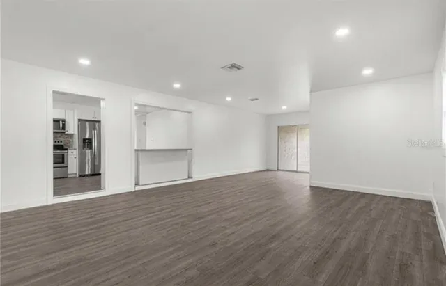 a view of an empty room with wooden floor and kitchen