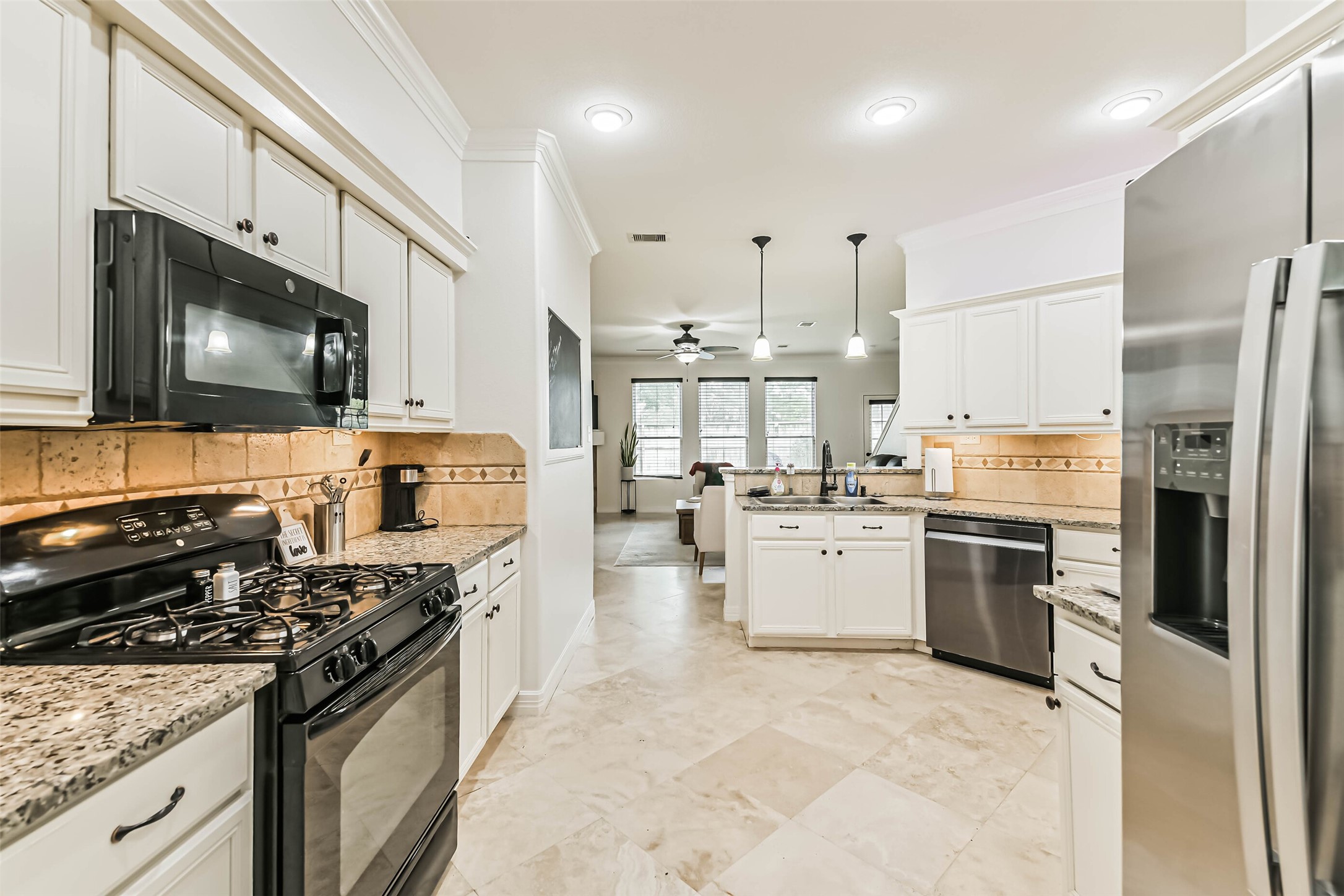 22538 Goss Spring Court Spring, TX 77373 - Photo 6 of 36 This is a modern, bright kitchen featuring white cabinetry, granite countertops, and stainless steel appliances, including a gas stove and double-door refrigerator. The open layout leads to a cozy living area with large windows, enhancing the spacious feel.