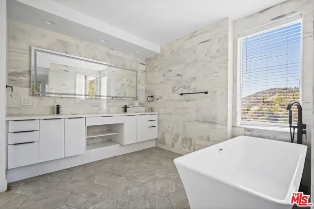 a large white bathroom with a sink a bathtub and next to a window