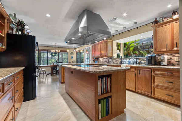 a kitchen with stainless steel appliances granite countertop a refrigerator a sink dishwasher a oven and a dining table with wooden floor