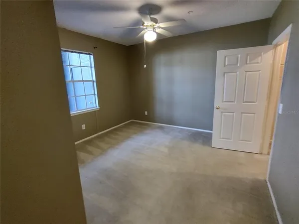 an empty room with chandelier fan and windows