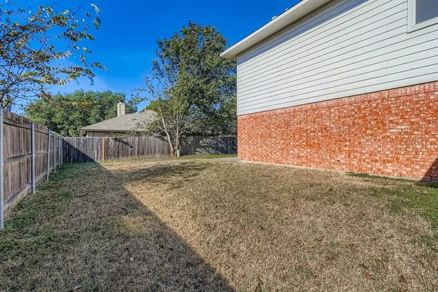 a view of a backyard with large trees and wooden fence