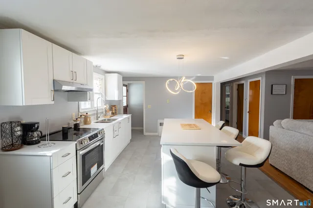 a large white kitchen with stainless steel appliances granite countertop a stove a sink a refrigerator white cabinets and wooden floor