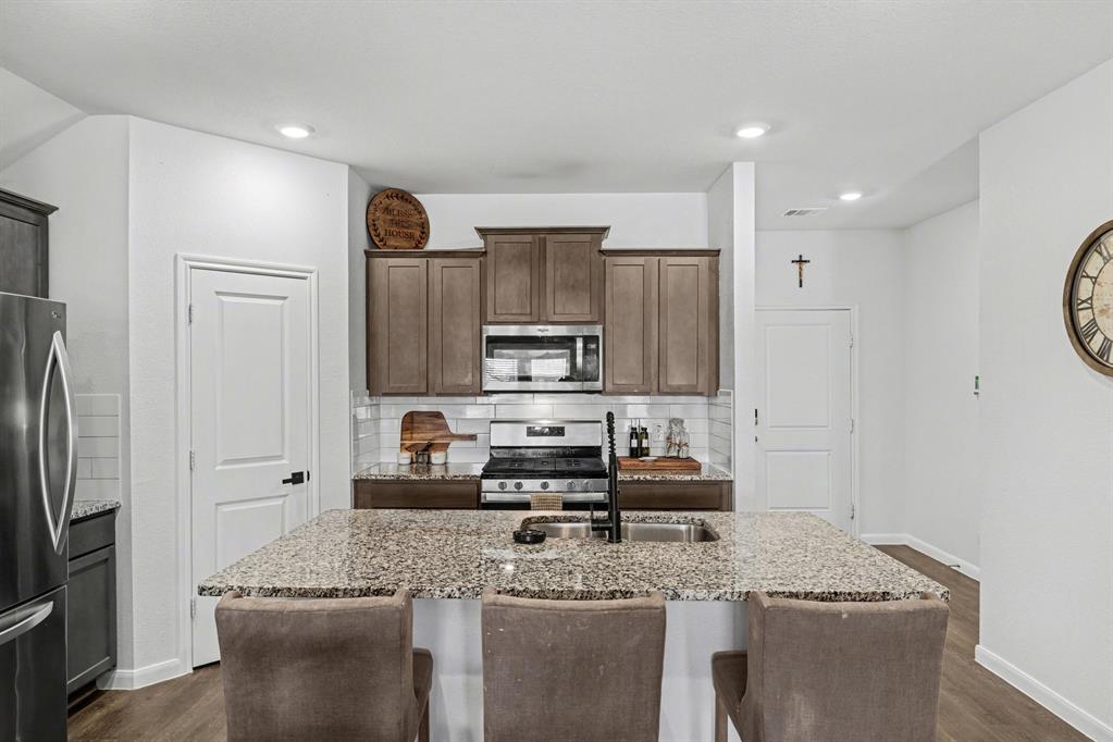 706 Spur Ridge Princeton, TX 75407 - Photo 11 of 36 Kitchen with stainless steel appliances, a kitchen breakfast bar, an island with sink, light stone counters, and recessed lighting