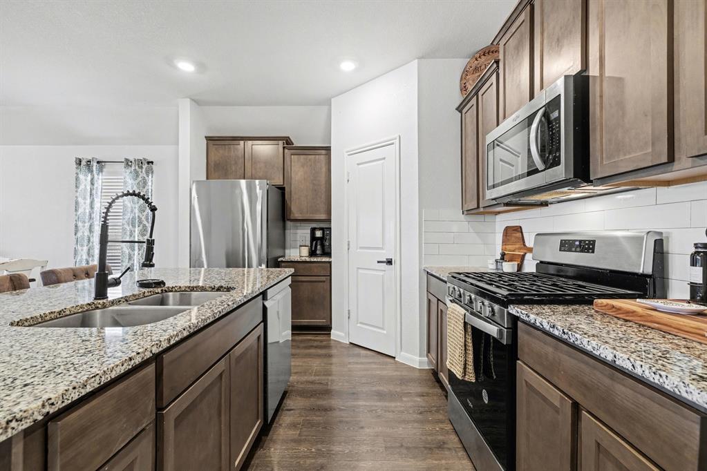 706 Spur Ridge Princeton, TX 75407 - Photo 18 of 36 Kitchen with stainless steel appliances, dark wood-style floors, light stone countertops, decorative backsplash, and dark wood finish cabinets