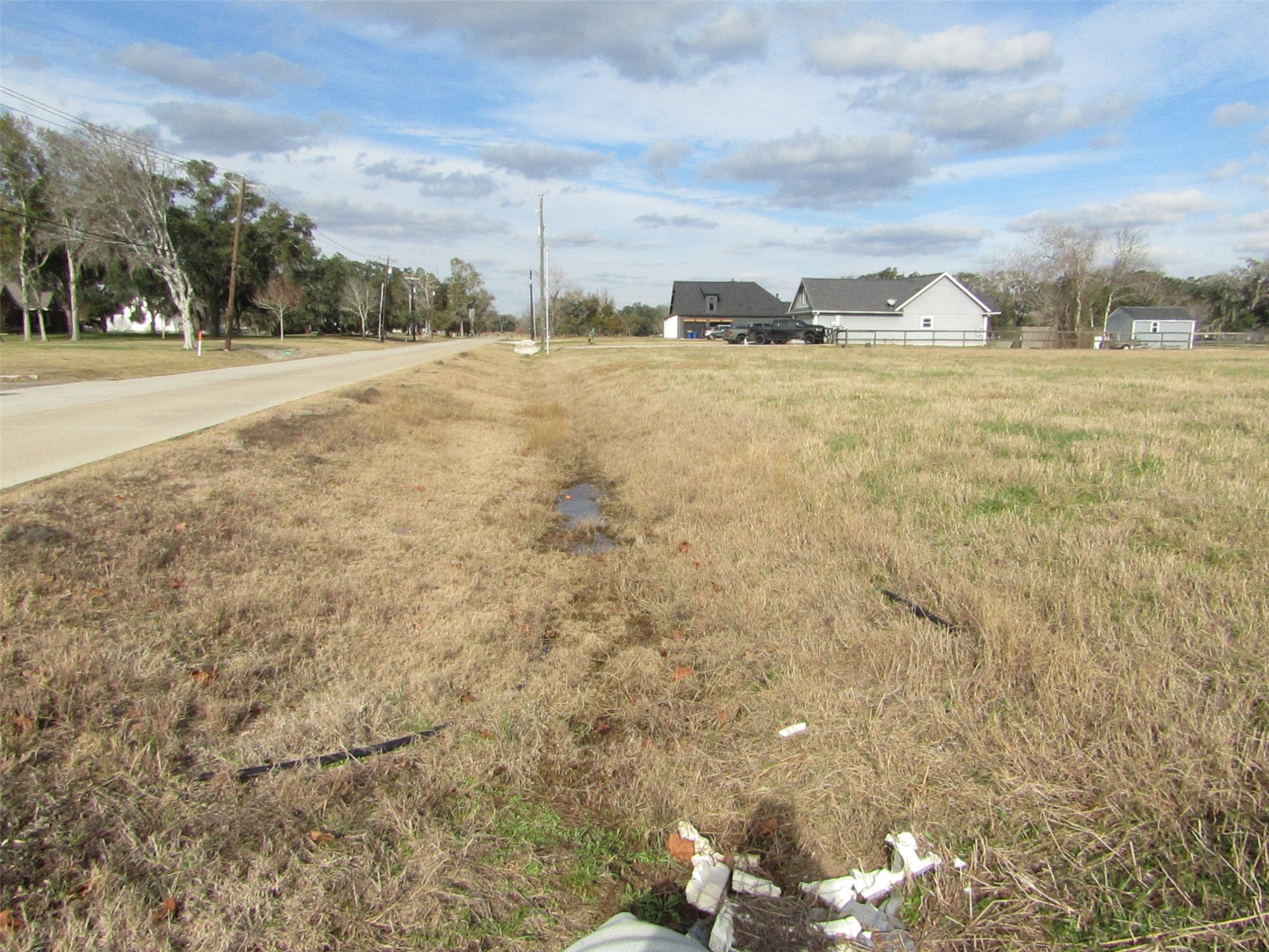 707 Winchester Trail Angleton, TX 77515 - Photo 3 of 8 Spacious, open lot with grassy terrain adjacent to a paved road. Nearby, there's a residential area with houses, providing a suburban feel. Ideal for building a custom home in a quiet neighborhood.