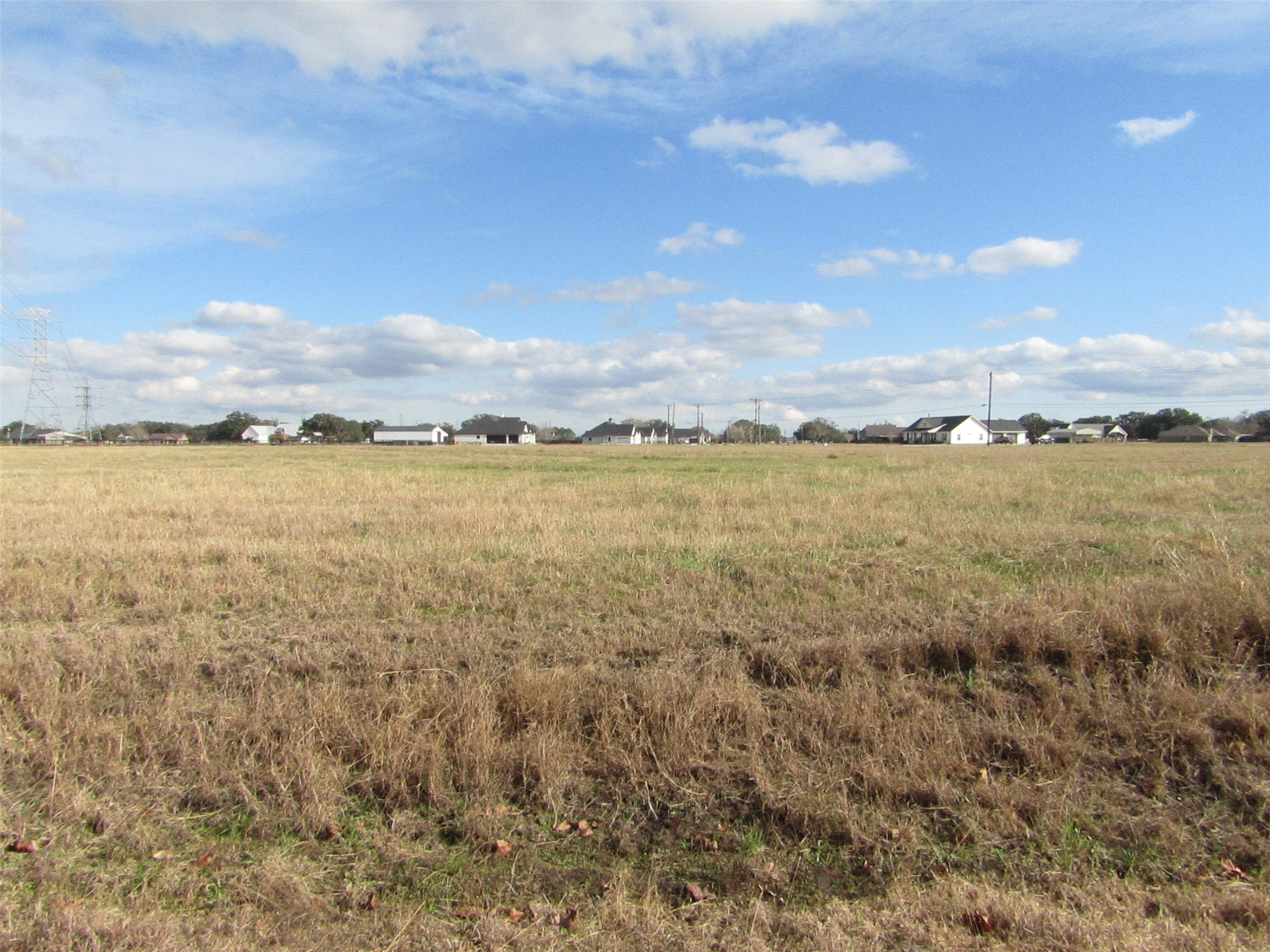 707 Winchester Trail Angleton, TX 77515 - Photo 5 of 8 Expansive open field with distant residential homes, offering a tranquil setting under a vast sky, ideal for potential building or development.