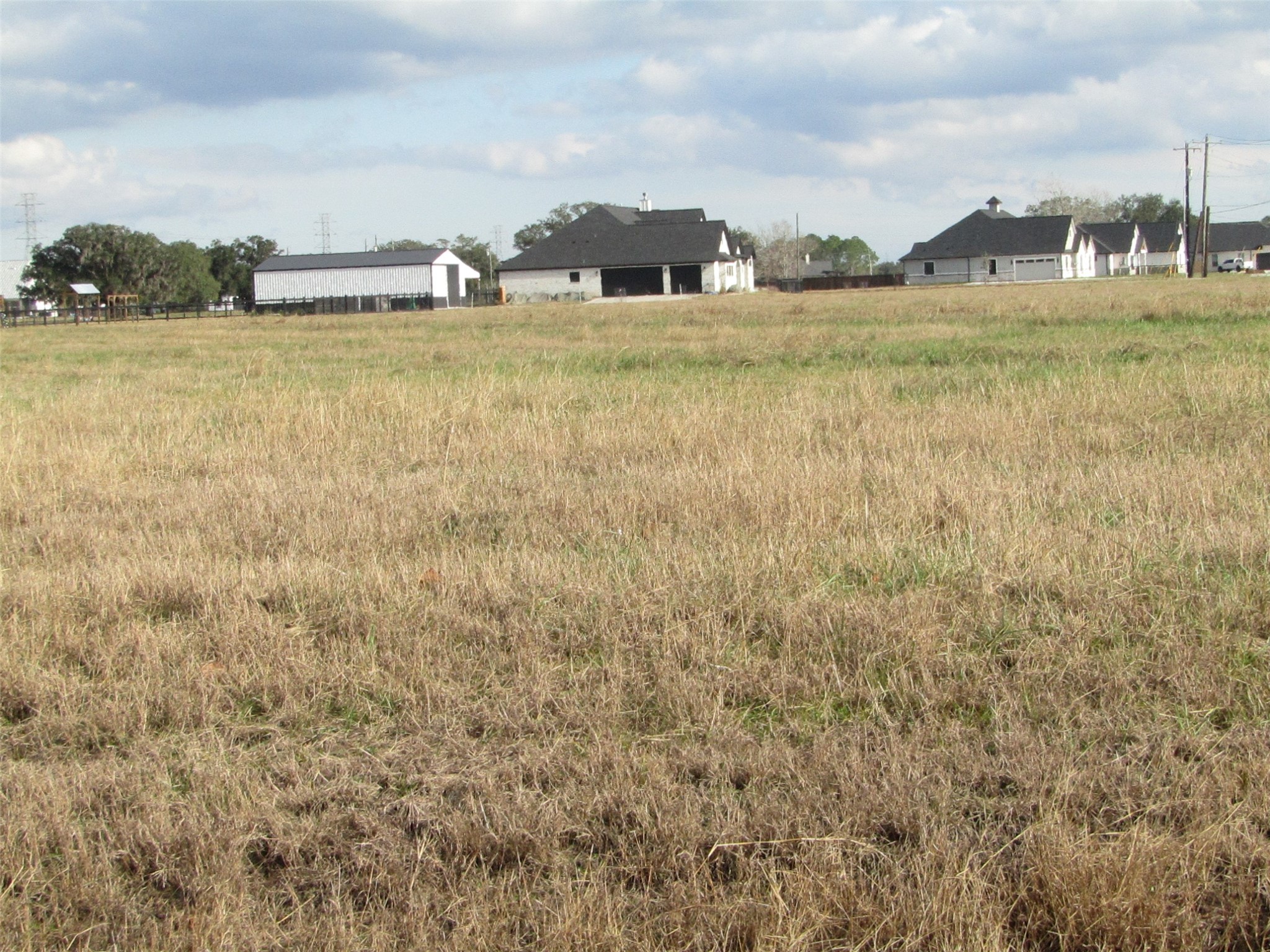 707 Winchester Trail Angleton, TX 77515 - Photo 8 of 8 Spacious, open field with a few nearby houses and barn-like structures, offering a rural atmosphere and plenty of potential for development.