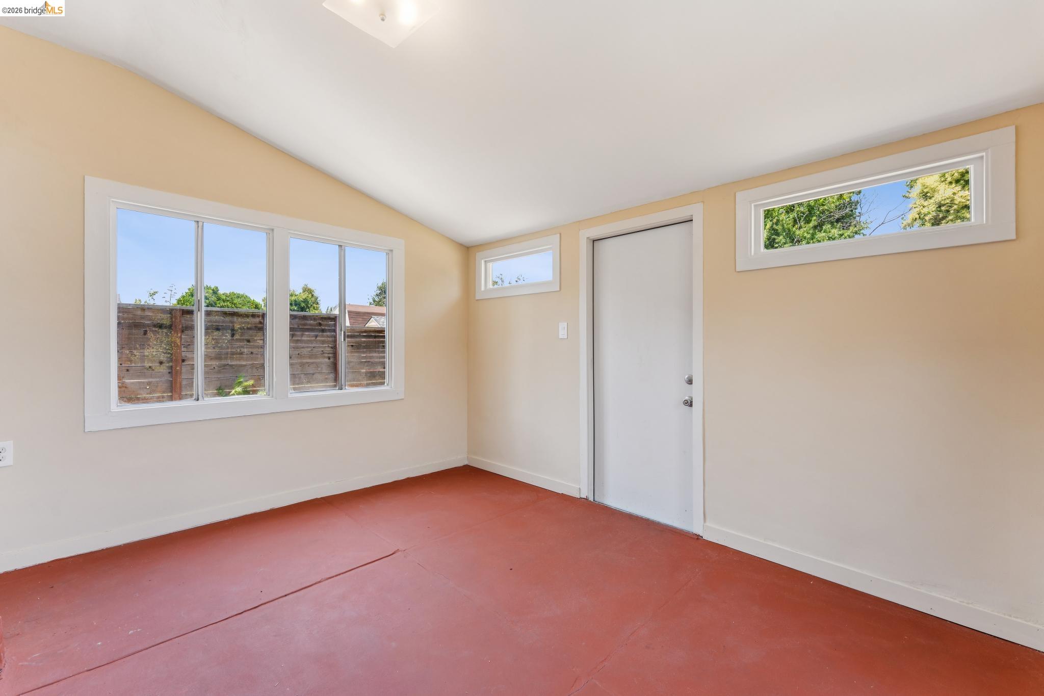 2879 Rheem Avenue Richmond, CA 94804 - Photo 23 of 45 Room featuring a vaulted ceiling, multiple windows, a white door, and red-toned flooring